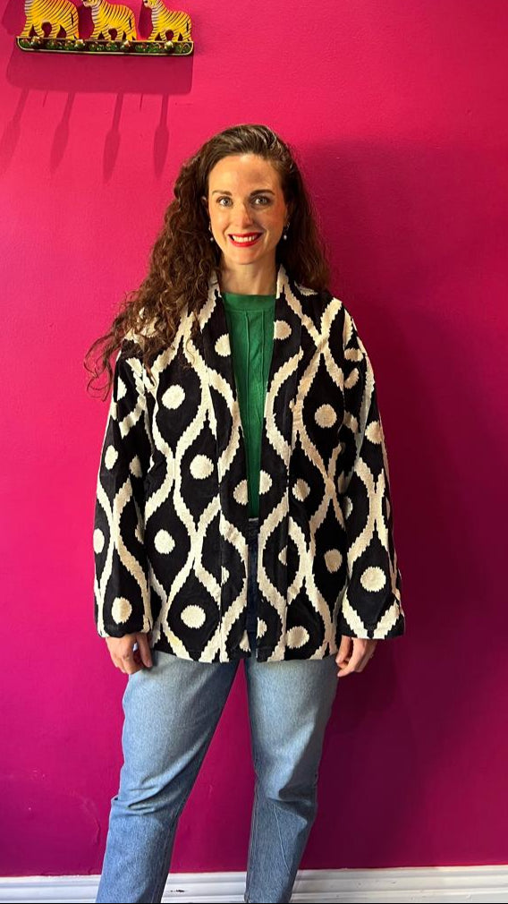 Woman wearing a patterned coat standing against a pink wall with three small yellow animals on a shelf.