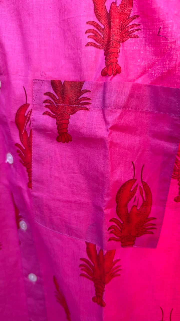 Bright pink fabric with red lobster illustrations and a pocket, photographed close up.