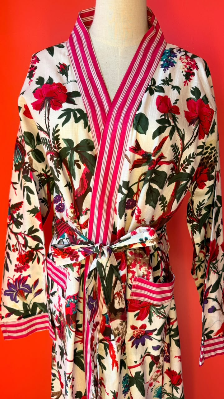 A floral print kimono-style robe with pink and white striped trim, displayed on a mannequin against a bright red background.