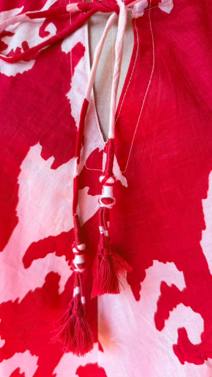 A close-up of a red and white abstract patterned garment with drawstrings and tassels at the neckline.