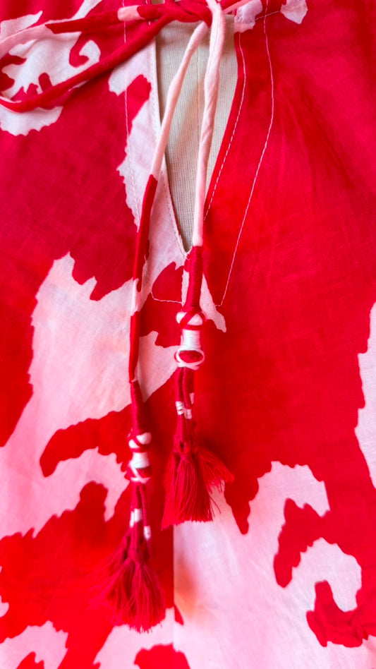 A close-up of a red and white abstract patterned garment with drawstrings and tassels at the neckline.