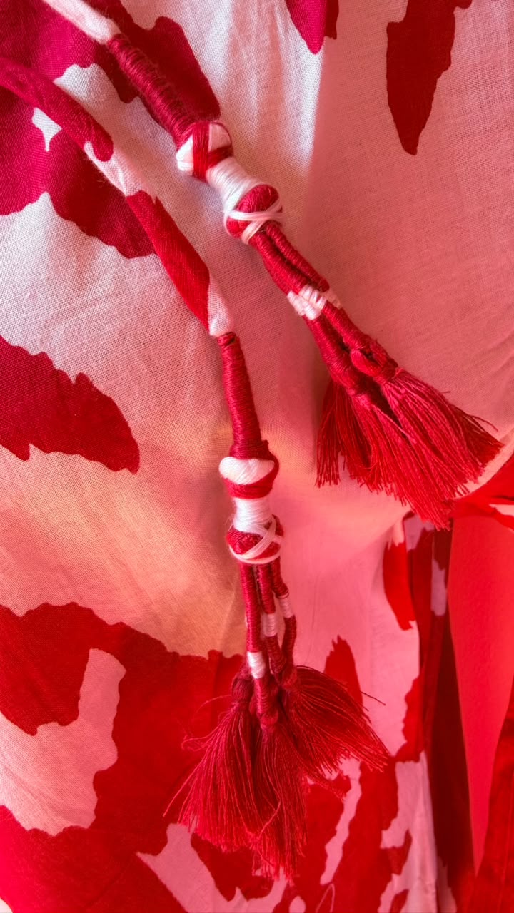 A close-up of a red and white patterned textile with braided cord details and tassels, filling the frame.