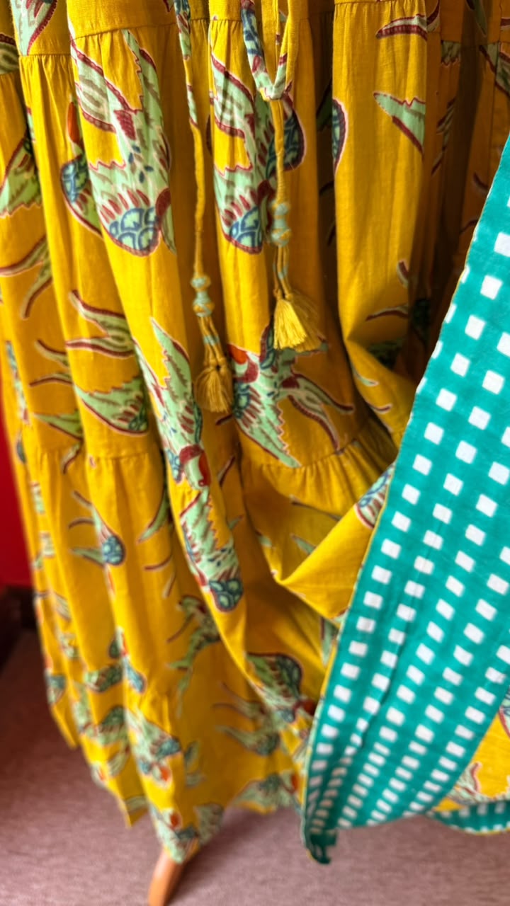 A close-up of a yellow tiered maxi dress with a colorful butterfly print, alongside a green and white checkered fabric.