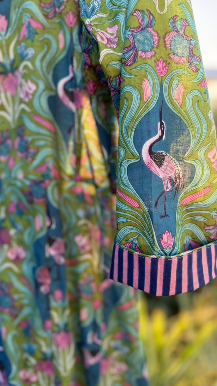 A close-up of a colorful printed garment featuring a pink flamingo motif on a teal and green background, with rolled cuffs showing a pink and navy striped inner lining.
