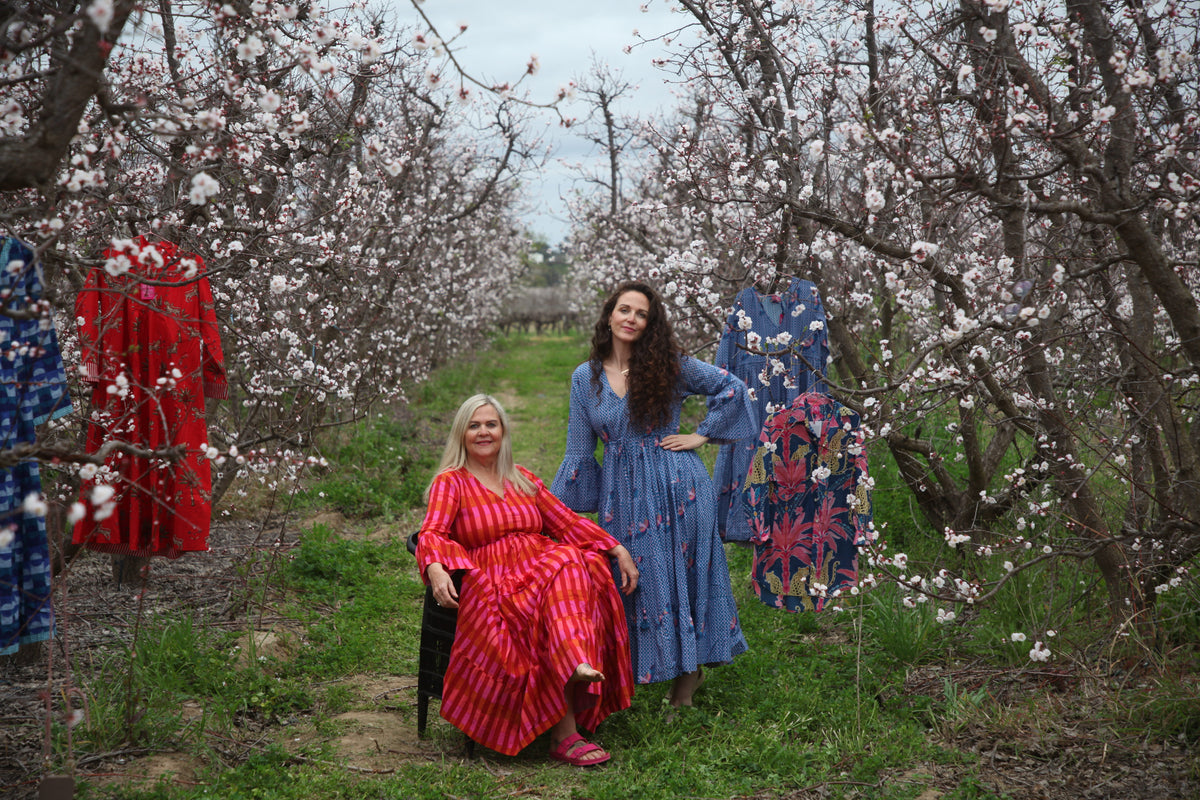 Two women modelling colourful Isabella cotton dresses in a blossoming orchard