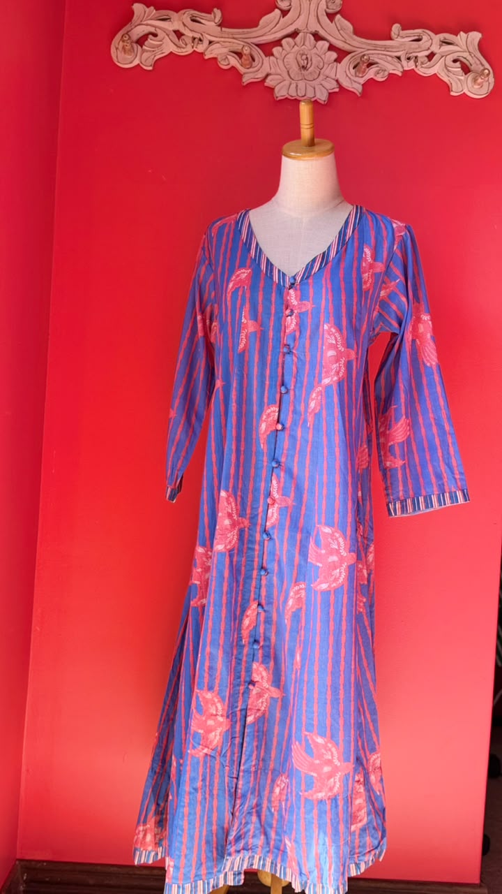 A blue and pink striped tunic dress with pink floral motifs, displayed on a mannequin against a bright red background.