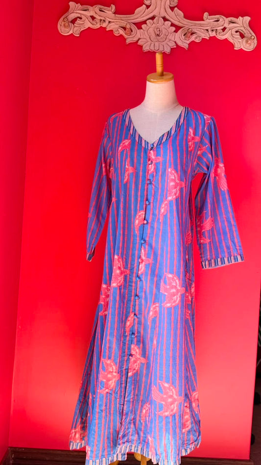 A blue and pink striped tunic dress with pink floral motifs, displayed on a mannequin against a bright red background.
