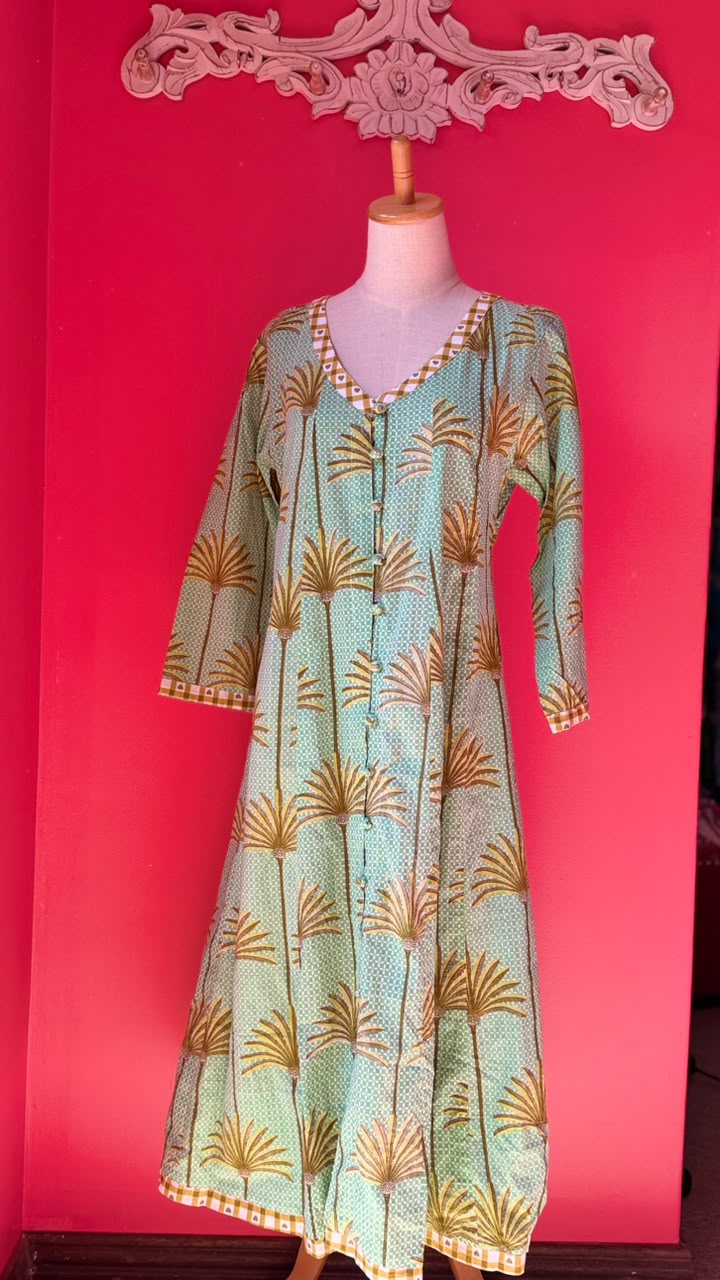 A light green and gold printed long kurta displayed on a dress form mannequin against a bright pink background.