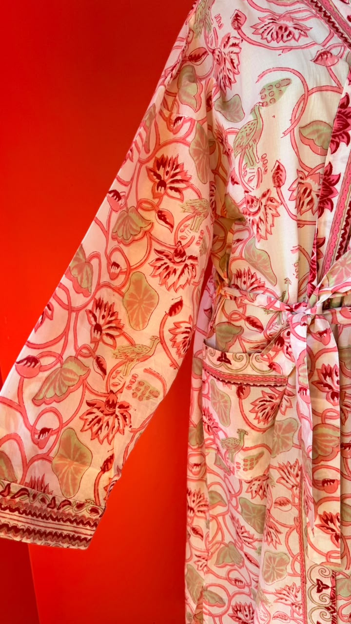 A close-up of a patterned robe or kimono-style garment with a tie belt, featuring red, pink, and beige botanical and floral motifs on a light base, set against a solid red background.