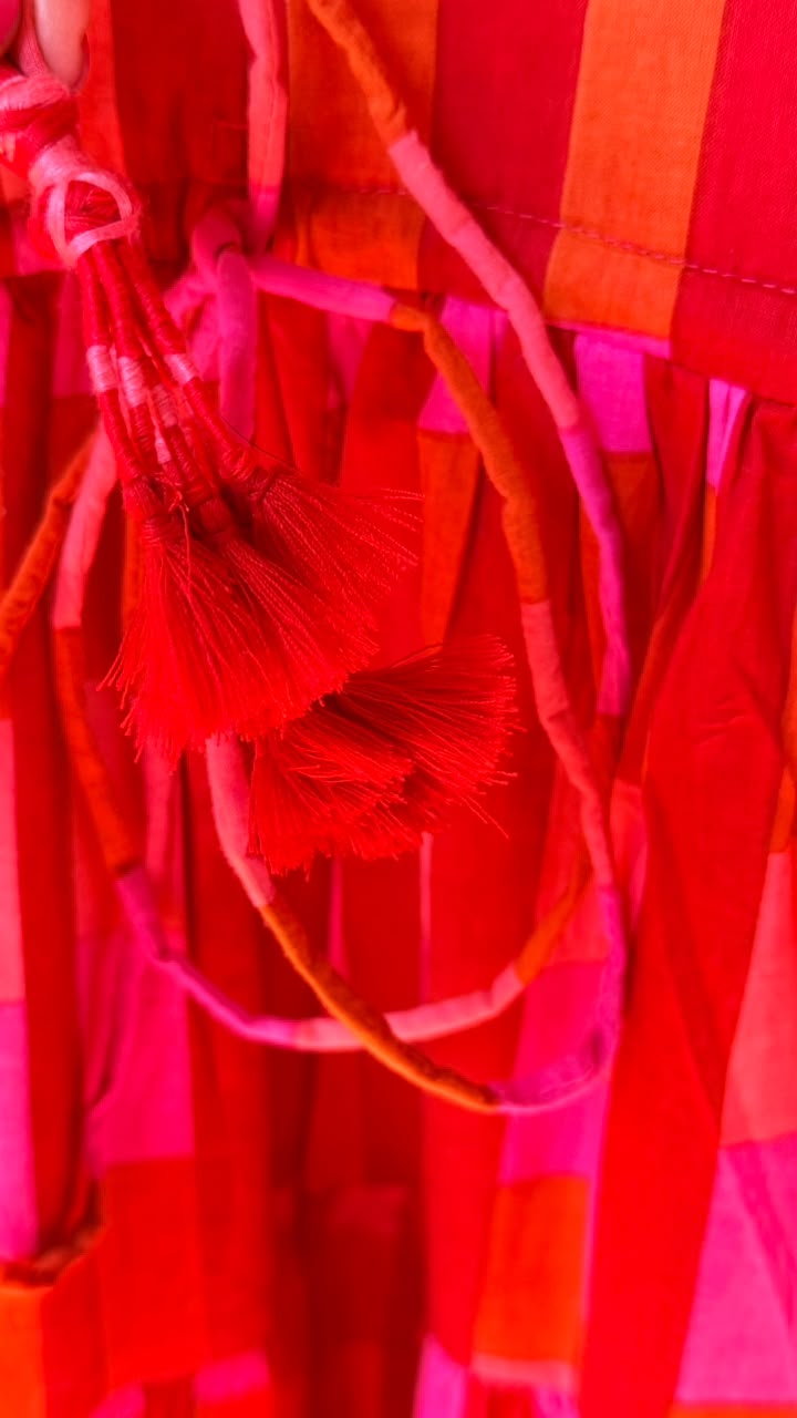 A close-up of a bright red and hot pink fringed textile or hanging ribbon decoration, with layered tassels and sheer strips filling the frame.
