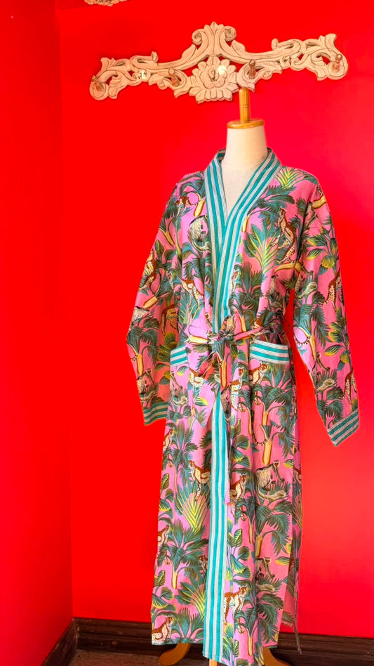 A pink tropical print robe with turquoise and white striped trim, displayed on a mannequin against a bright red wall.