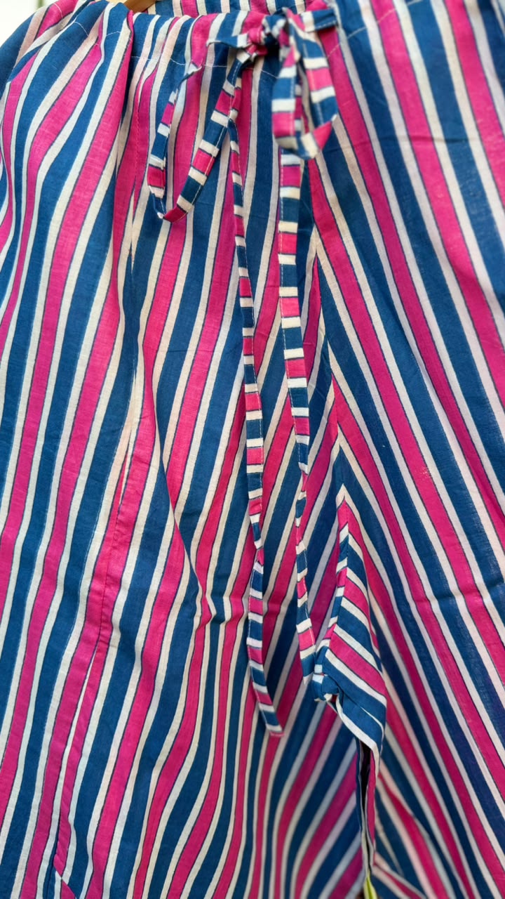 A close-up of a striped textile with vertical pink, navy blue, and off-white stripes, featuring a tie detail at the top.