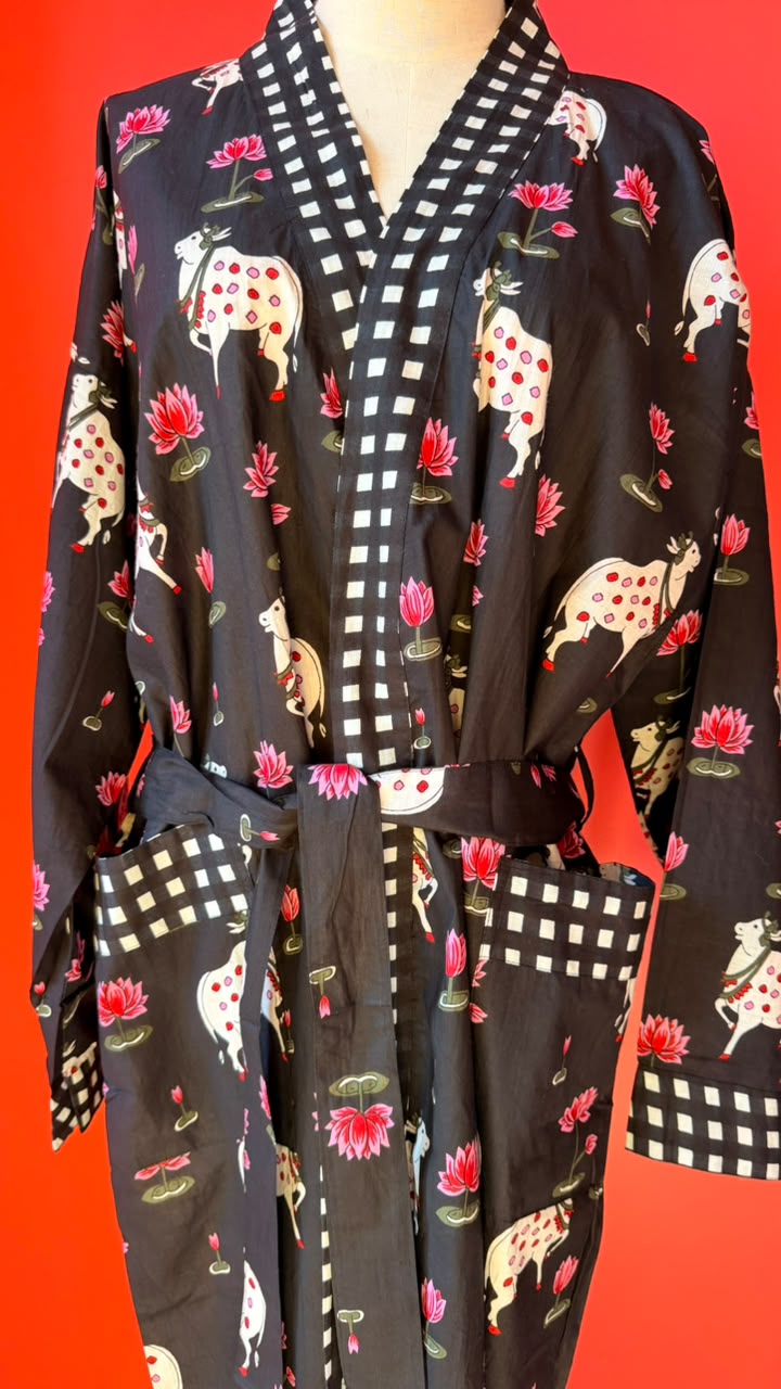 A black kimono-style robe with a white and red checkered collar and hem, featuring a pattern of white deer with red spots, pink lotus flowers, and green leaves. The robe is shown against a solid red background.