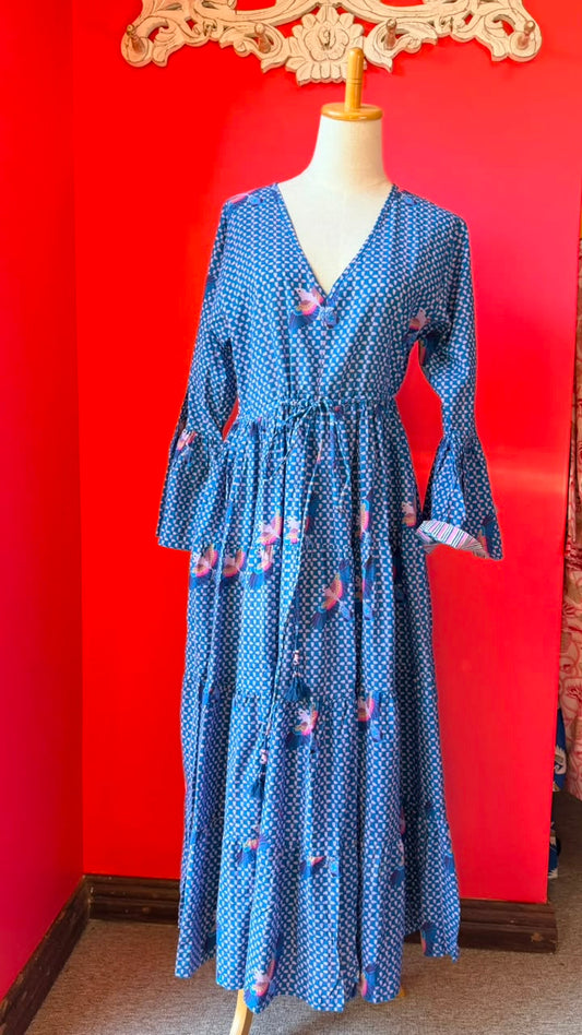 A blue long-sleeve midi dress with a white polka dot pattern and pink floral accents, displayed on a mannequin against a bright red wall.