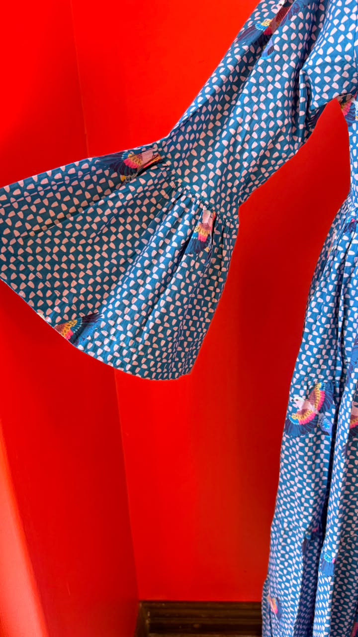 A close-up of a blue patterned garment with a geometric print and small pink floral accents, shown against a vivid red background.